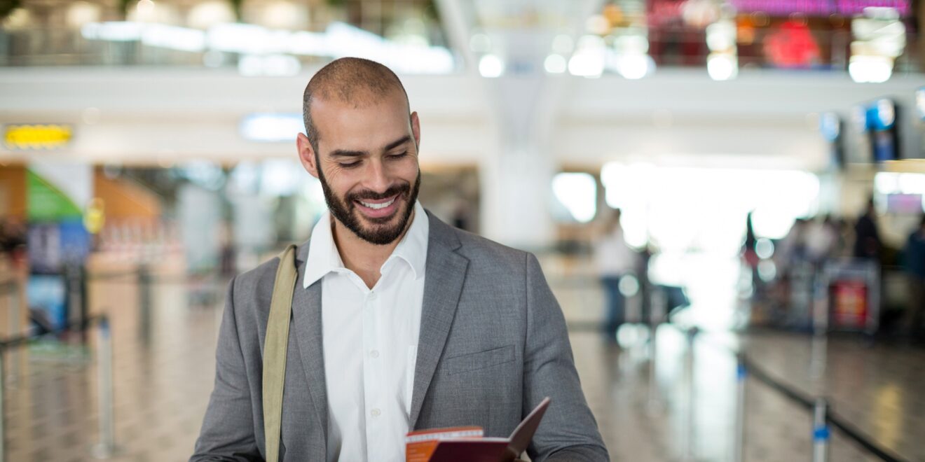 smiling businessman holding boarding pass checking his mobile phone