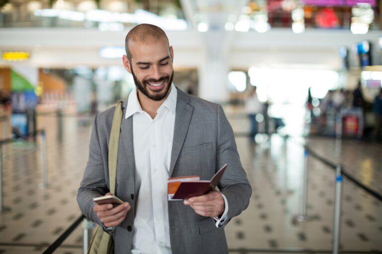 smiling businessman holding boarding pass checking his mobile phone