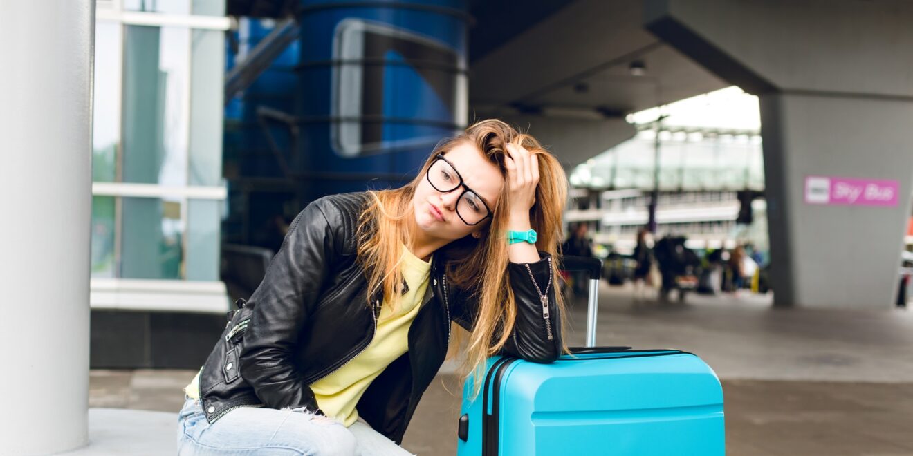 portrait pretty girl with long hair glasses sitting outside airport she wears yellow sweater with black jacket jeans she leaned suitcase is bored waiting